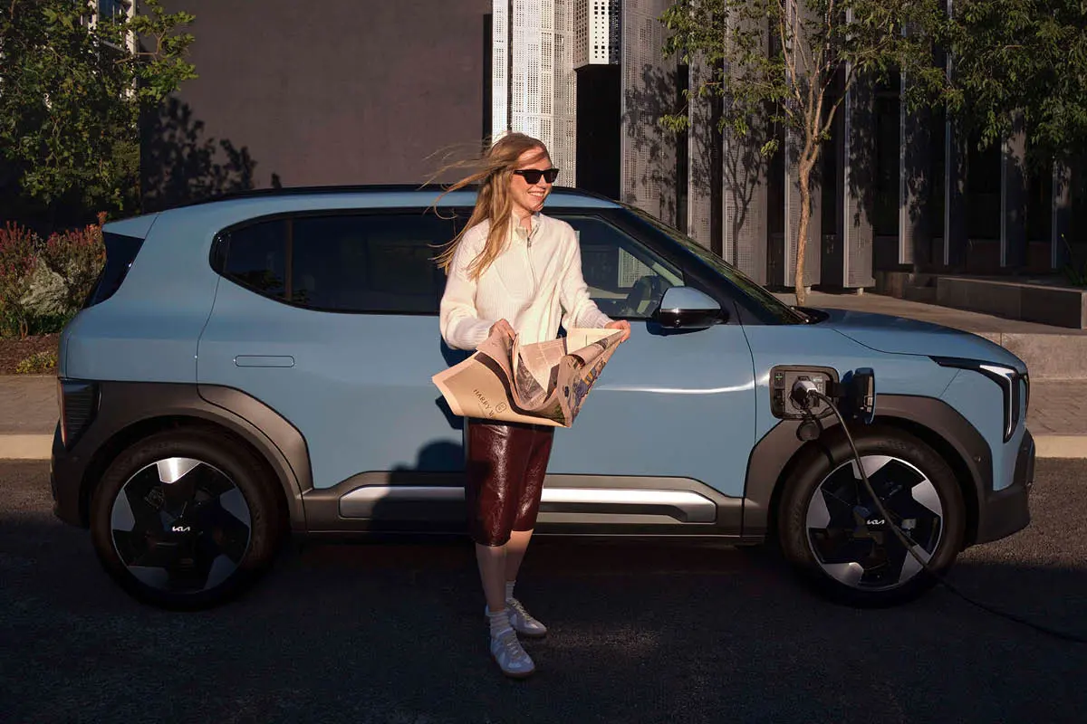 Junge Frau steht Zeitung haltend neben Kia EV2 Modell während es läd