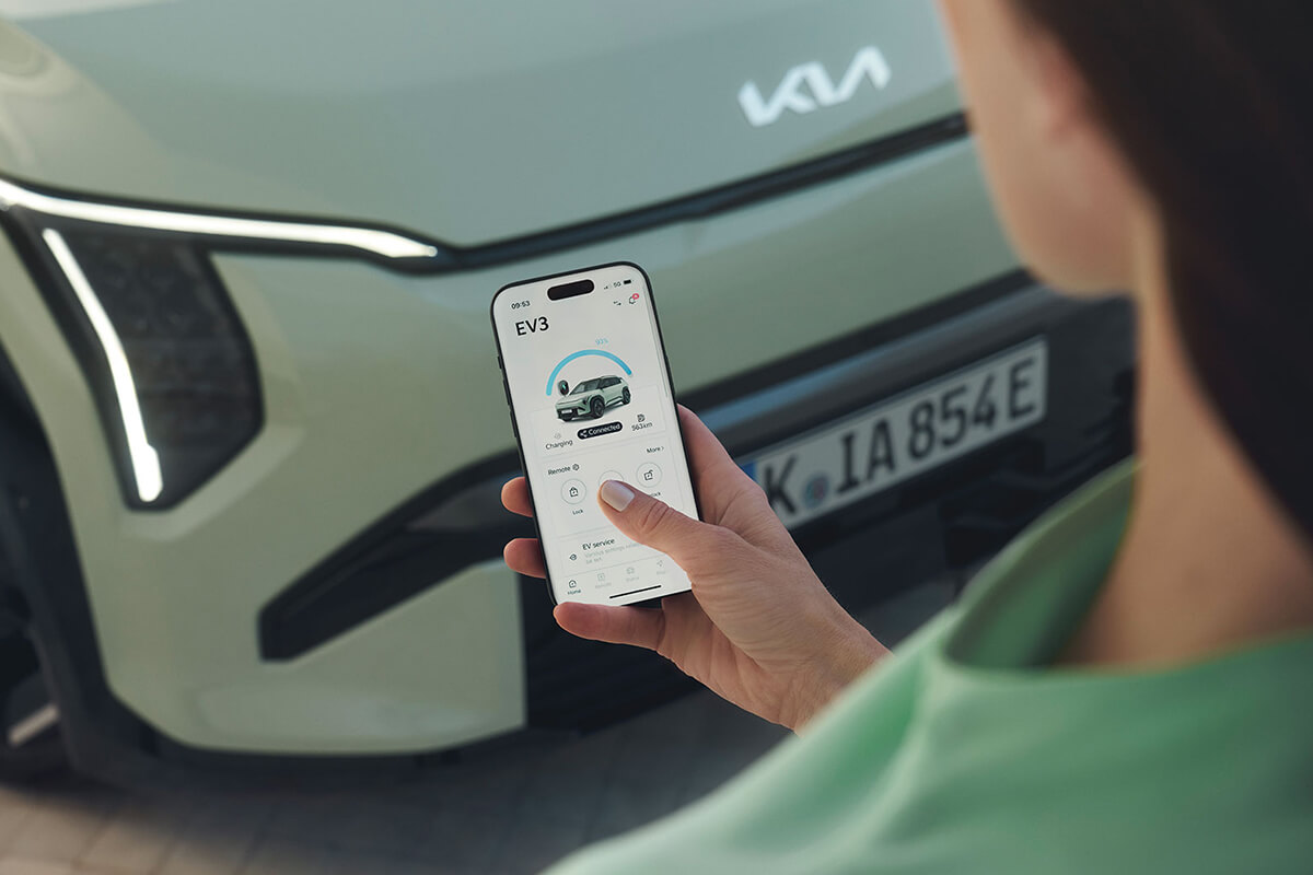 Man sieht eine Person mit dem Handy vor dem Kia EV3 und der Steuerungsapp von Kia.