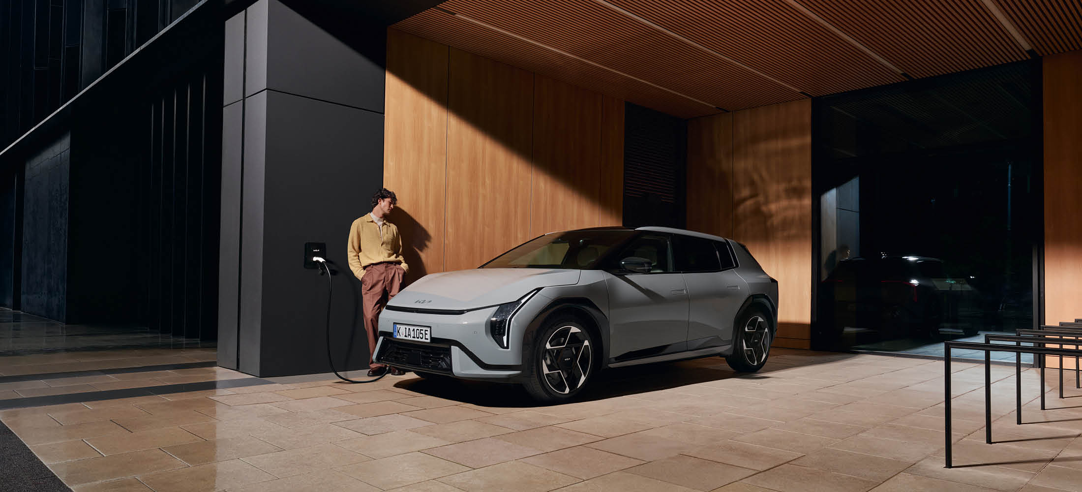 Mann steht in seiner Einfahrt und sein Kia EV4 wird geladen an integrierter Ladebox in der Wand