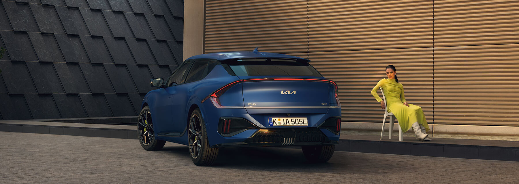 Kia EV6 GT Heckansicht, parkend, mit einer Frau, die daneben auf einem Stuhl sitzt