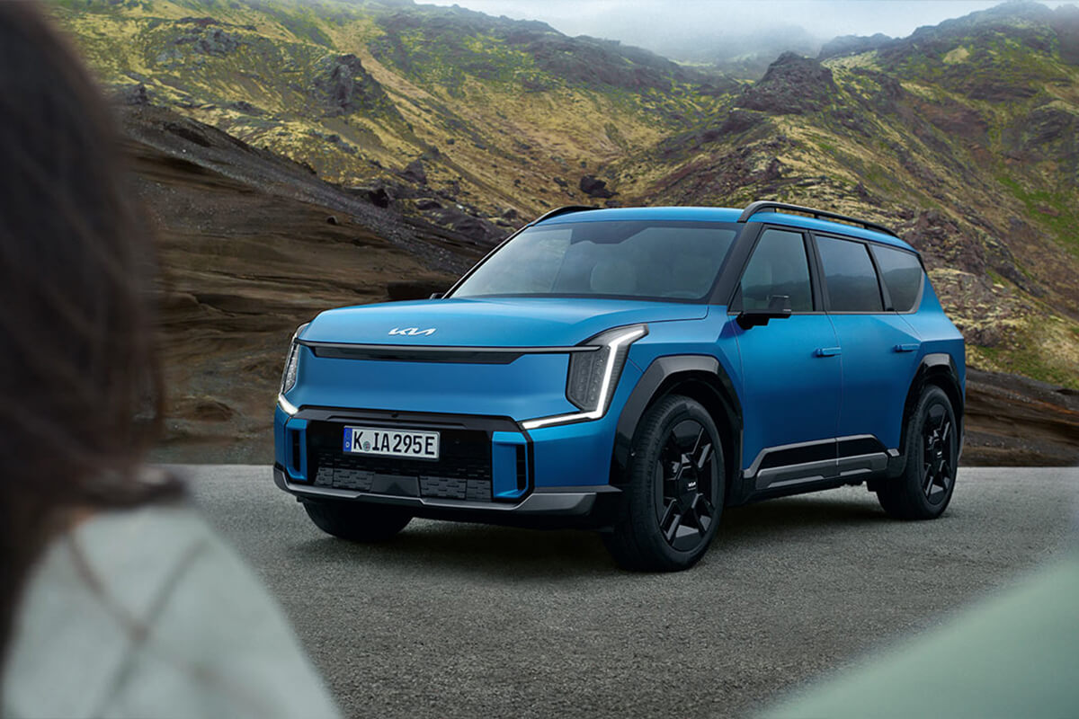 Man sieht den Kia EV9 GT-Line, im Hintergrund Berge und am Bildrand ist eine Person angeschnitten zu erkennen.