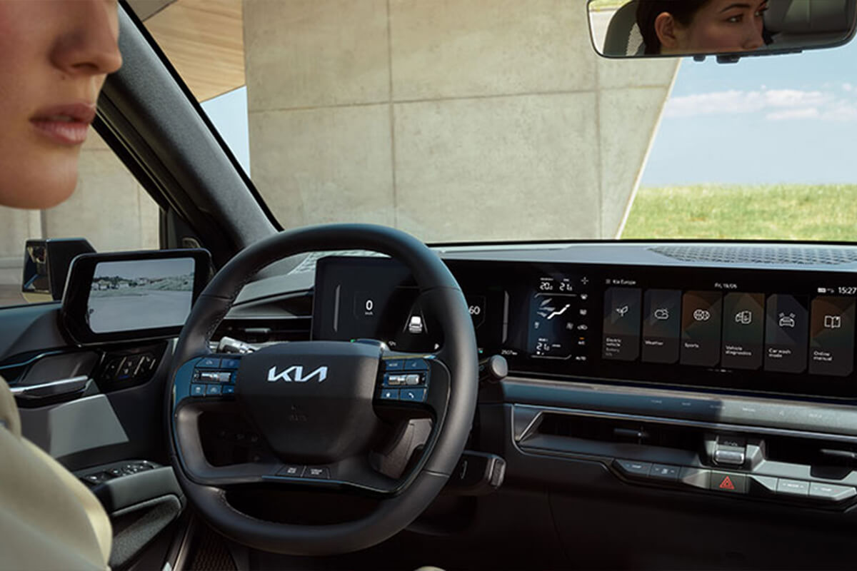 Man sieht den Fahrerraum eines Kia EV9; am Bildrand ist eine Frau angeschnitten zu erkennen.
